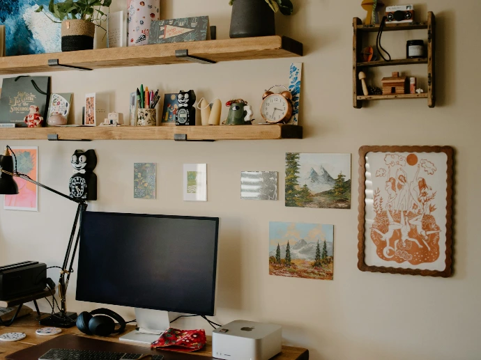 Desk with computer, shelves, and artwork on wall.